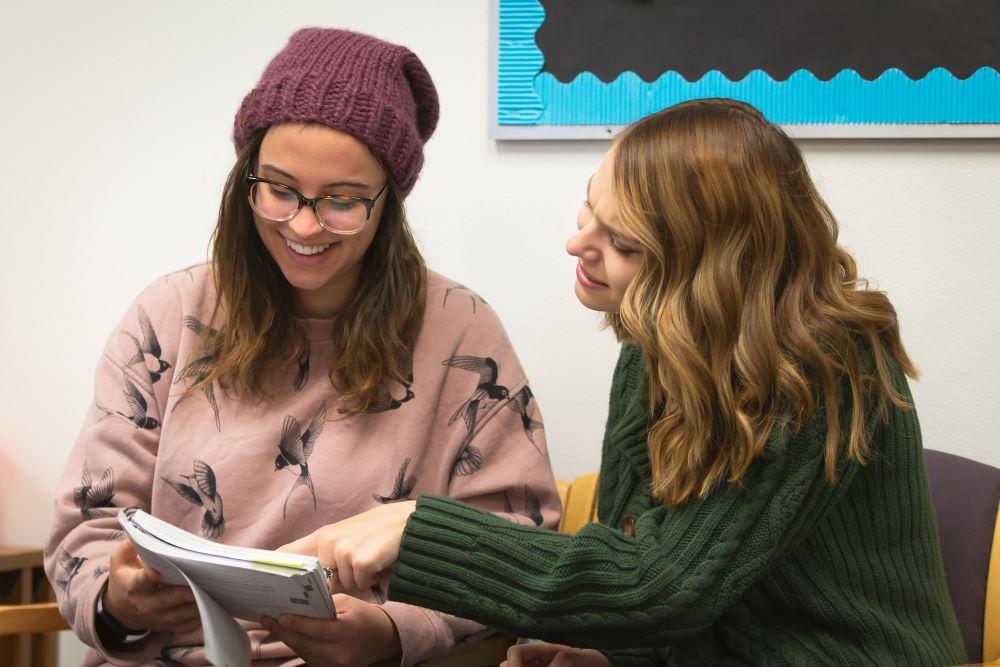 two women sitting, talking, and looking at a notebook